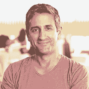 A man with short hair and a slight smile stands indoors, wearing a plain T-shirt. The background is softly blurred, showing people and a bright window. The image uses a warm, stylized color filter, capturing the supportive spirit of NBIS—Nanaimo Brain Injury Society.