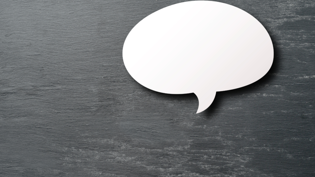 A blank white speech bubble cutout lies on a dark gray slate surface, positioned in the top right corner—an inviting space for communication and awareness, perfect for sharing messages from the Nanaimo Brain Injury Society (NBIS).